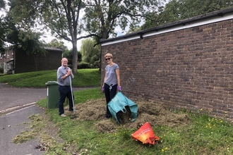 Two volunteers raking grass area to prepare for Wildflower community plot