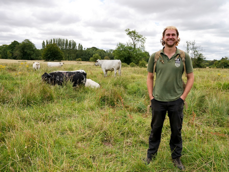 Reserves officer sam to right of image smiling, in background to sam's left is 4 cows