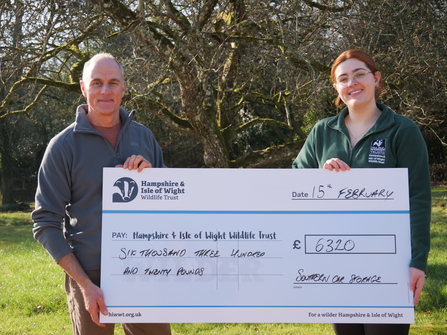 Alan from Southern Car Storage and lauren from HIWWT fundraising team holding giant check outside in a green space