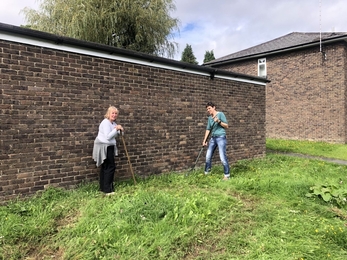 Two volunteers raking grass area to prepare for Wildflower community plot