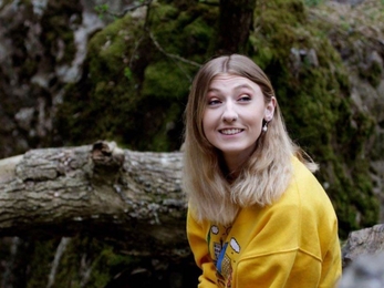 Georgina sat in the wood, smiling, looking off into the distance