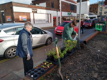 Volunteers standing in area of raised beds next to high street doing some gardening