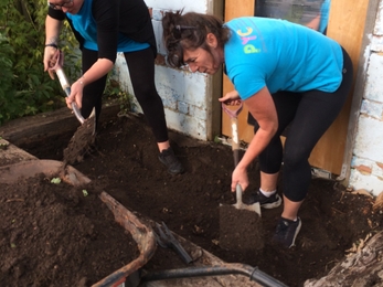 Two woman digging soil out of a raised wooden bed.