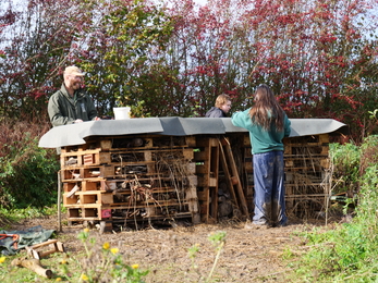 Three people attaching the felt roof onto a big bug hotel 