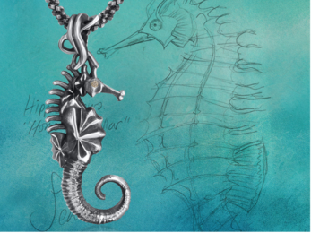 Silver seahorse pendant on a teal background with a seahorse drawn with pencil on it. 