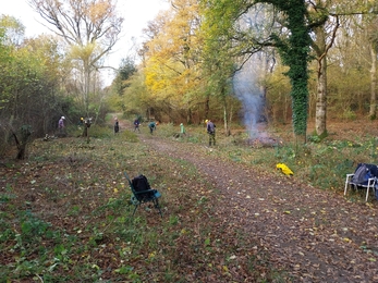 Several volunteers carrying out conservation tasks in the background. A small bonfire burns on the right 