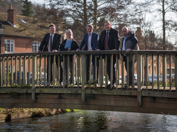 5 people line up on a bridge over a chalk stream in a semi urban environment