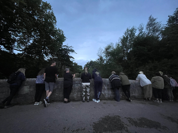 A group of people peering over a stone bridge at night time 