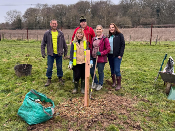 a group of 5 adults posing for a photo at a tree planting