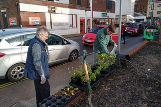 Volunteers standing in area of raised beds next to high street doing some gardening
