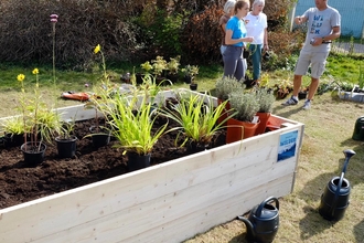 Raised bed with plant pots in position to be planted. In the background, Andy discusses with residents. 