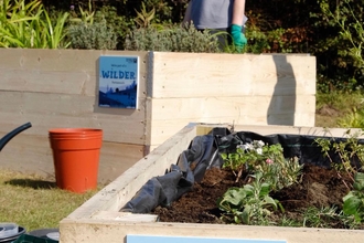 Close up of the raised beds with plaques nailed on to their sides. Plaques read "We're part of a Wilder Portsmouth"