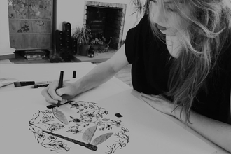 Black and white image of artist leaning over paper and drawing