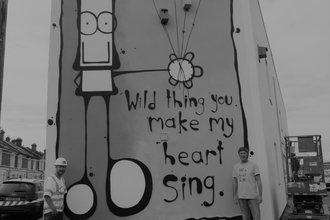 Street mural of cartoon man holding balloons which are actually bird boxes. The words, "Wild thing, you make my heart sing" are painted, too.