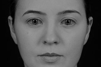 Black and white photo of woman staring at camera. Hair is pulled back and irises in her eyes resemble tree rings.