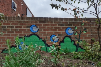 View of raised bed with plants. In the back there's a brick wall with a mural of birds, painted by FARK