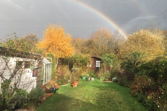 Back garden with wildlife borders. Grey skies, but a rainbow flying across the sky brightens up the garden.