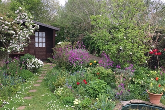 Stepping stones weaving through a garden, between wildflower beds. Path leads to wooden summer house