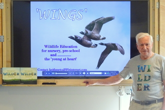 Man (Keith Metcalf) standing in front of projector screen. Screen shows three geese flying to the left.