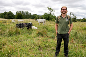 Reserves officer sam to right of image smiling, in background to sam's left is 4 cows