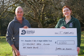 Alan from Southern Car Storage and lauren from HIWWT fundraising team holding giant check outside in a green space