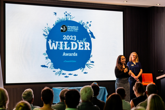Wilder Awards Megan McCubbin and Debbie Tann on stage in front of the award logo