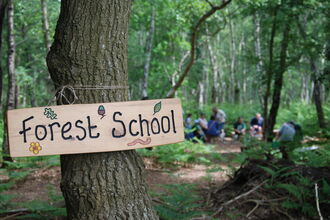 Forest School wooden plaque on tree with people in background
