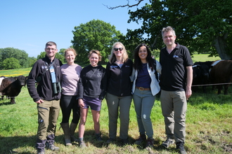Several individuals standing in a grassy field under a clear blue sky.