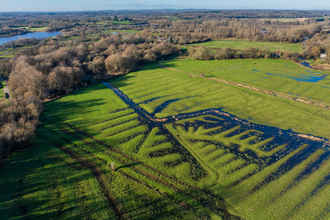 Aerial view of a lush, green landscape with a network of water channels and surrounding trees, under a clear blue sky.