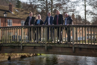 5 people line up on a bridge over a chalk stream in a semi urban environment