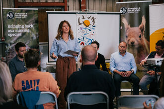 A woman standing in front of a whiteboard presenting to a seated crowd of people 