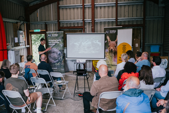 A seated wall crowd watching a presentation on a projector screen
