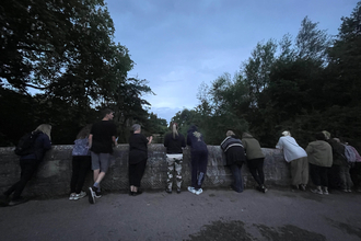 A group of people peering over a stone bridge at night time 