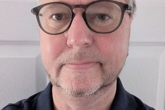 Man with glasses on, looking at the camera smiling. 