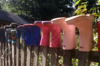 Wellington boots in a line upside down along the top of a fence,