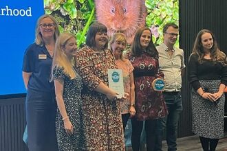 A group of 7 people on a stage posing for a group photo for an award they have won