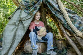 Girl sitting in a woodland den holding an animal toy.
