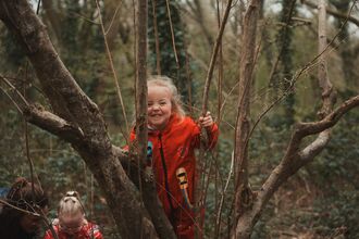 Smiling girl in red rainsuit climbing a tree.