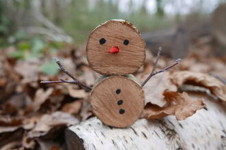 A snowman made of log slices sitting on a log in a woodland.