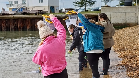 Group of adults on the beach standing in shallow water with Plankton nets
