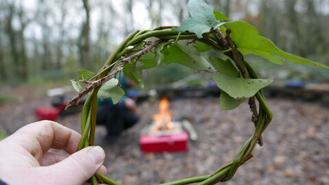 Hand holding a hazel and ivy wreath ring by a campfire
