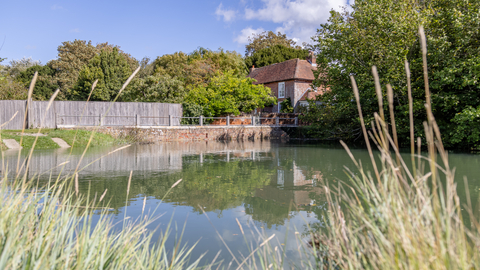 A body of water with a brick building in the near background on a sunny day 