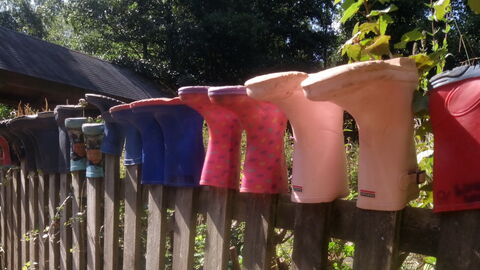 Wellington boots in a line upside down along the top of a fence,