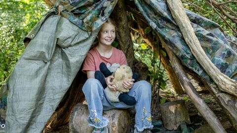 Girl sitting in a woodland den holding an animal toy.