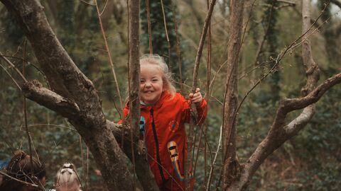 Smiling girl in red rainsuit climbing a tree.
