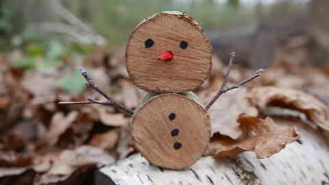 A snowman made of log slices sitting on a log in a woodland.