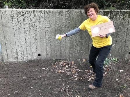 Woman in yellow t-shirt and black trousers sprinkling seeds on soil