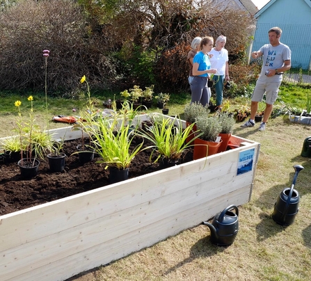 Raised bed with plant pots in position to be planted. In the background, Andy discusses with residents. 