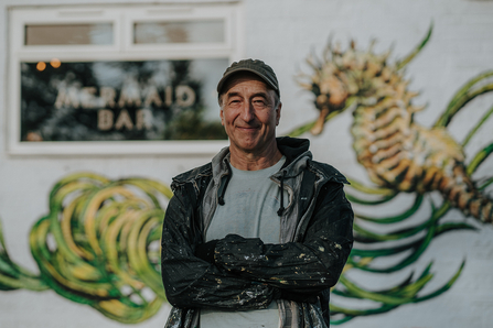 Artist ATM stands in front of completed seagrass mural © Adrift 