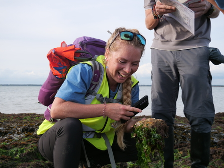 Emily holding a rock and her phone identifying a sea squirt